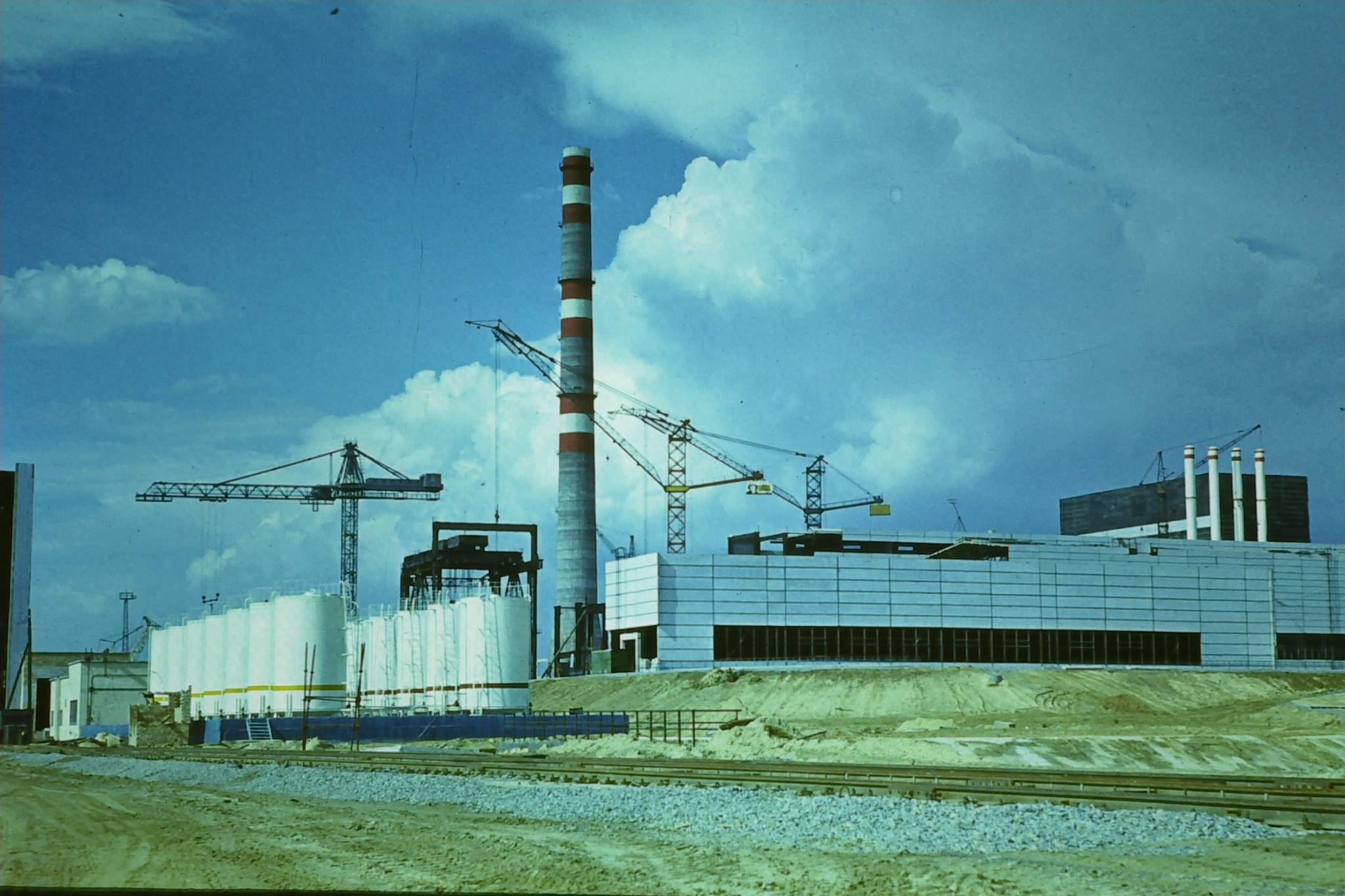 W środku kadru widoczny komin wentylacyjny bloków energetycznych nr I i II. Po prawej budynek główny reaktora i maszynownia bloku energetycznego nr I w trakcie prac budowlanych.